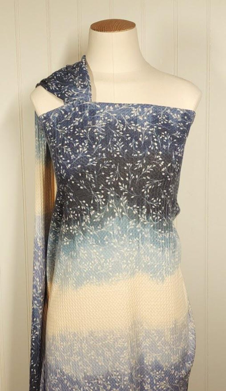 May include: A blue and white patterned fabric draped over a mannequin. The fabric has a gradient effect, changing from dark blue at the top to a light cream colour at the bottom. The pattern includes small white floral sprigs.