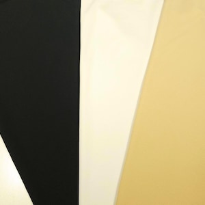 May include: Three distinct vertical panels of fabric displayed side by side. The left panel is solid black, the centre panel is solid white, and the right panel is a solid light tan or beige colour. Each section features a smooth, matte texture.