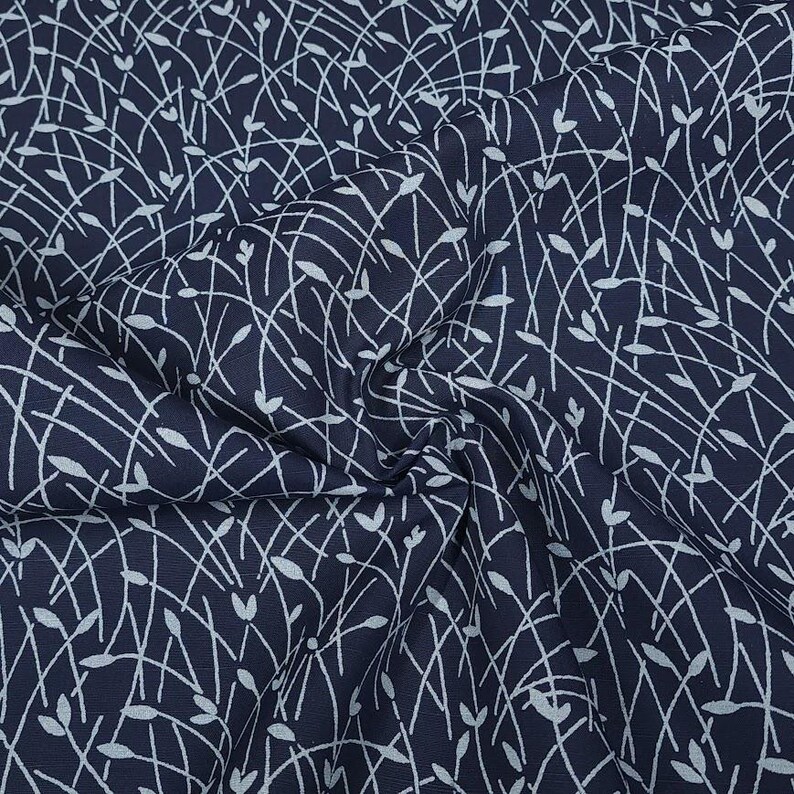 May include: Dark navy fabric with a white, delicate, leaf-like pattern. The design features intersecting lines and small, stylized leaf shapes, creating a textured and flowing visual effect. The fabric is slightly wrinkled.