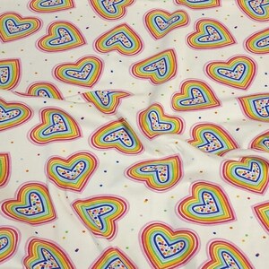 K&ouml;nnte beinhalten: Wei&szlig;er Stoff mit einem sich wiederholenden Muster aus regenbogenfarbenen Herzen. Jedes Herz ist rosa umrandet und mit einem gepunkteten Design gef&uuml;llt. Die Herzen sind mit Regenbogenfarben geschichtet und mit kleinen Punkten &uuml;bers&auml;t.