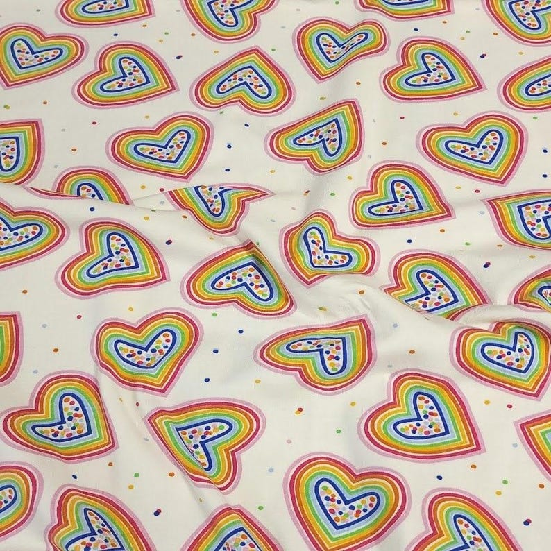 K&ouml;nnte beinhalten: Wei&szlig;er Stoff mit einem sich wiederholenden Muster aus regenbogenfarbenen Herzen. Jedes Herz ist rosa umrandet und mit einem gepunkteten Design gef&uuml;llt. Die Herzen sind mit Regenbogenfarben geschichtet und mit kleinen Punkten &uuml;bers&auml;t.