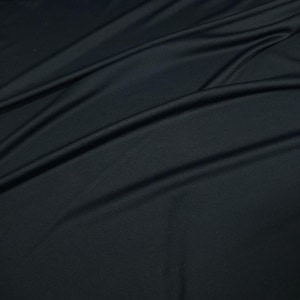 May include: A close-up shot of a dark, possibly black, fabric with a smooth, flowing texture. The fabric has subtle folds and creases, creating shadows and highlights that add depth. The material appears to be soft and drapes naturally.