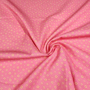 May include: A pink fabric featuring a repeating pattern of small, light yellow five-petaled flowers. The material is gathered in the center, creating soft folds and drapes that highlight the consistent distribution of the floral print across the surface.
