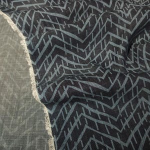 Puede incluir: Primer plano de una tela azul oscuro con un patr&oacute;n geom&eacute;trico repetitivo en azul claro. La tela tiene un borde sin rematar. El patr&oacute;n consiste en l&iacute;neas anguladas y peque&ntilde;os trazos horizontales, creando una apariencia texturizada.