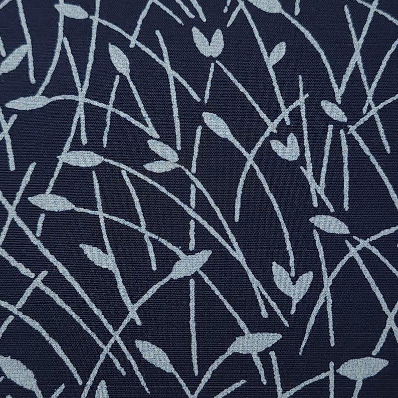 May include: Close-up of a navy blue fabric with a repeating pattern of light blue, stylized plant stems and leaves. The design features thin, curved lines and oval and heart-shaped leaf forms, creating a textured, organic aesthetic.