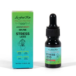May include: A Free Kin Stress Less essential oil bottle with a dropper. The bottle is green and black with white text. The bottle is labeled "100% Pure" and "Aromatherapy". The bottle is sitting on a white surface.