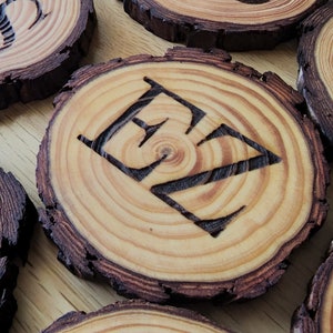 May include: Wooden coasters with the letters "EZ" burned into the surface. The coasters are round and have a natural wood finish.