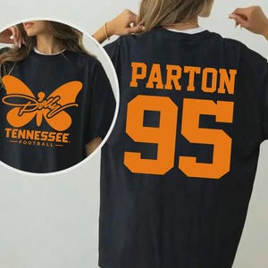 May include: A black t-shirt featuring an orange graphic of a butterfly with the text Dolly Tennessee Football on the front and the orange text Parton 95 on the back. The design uses a bold, athletic font for the number and name on the back.