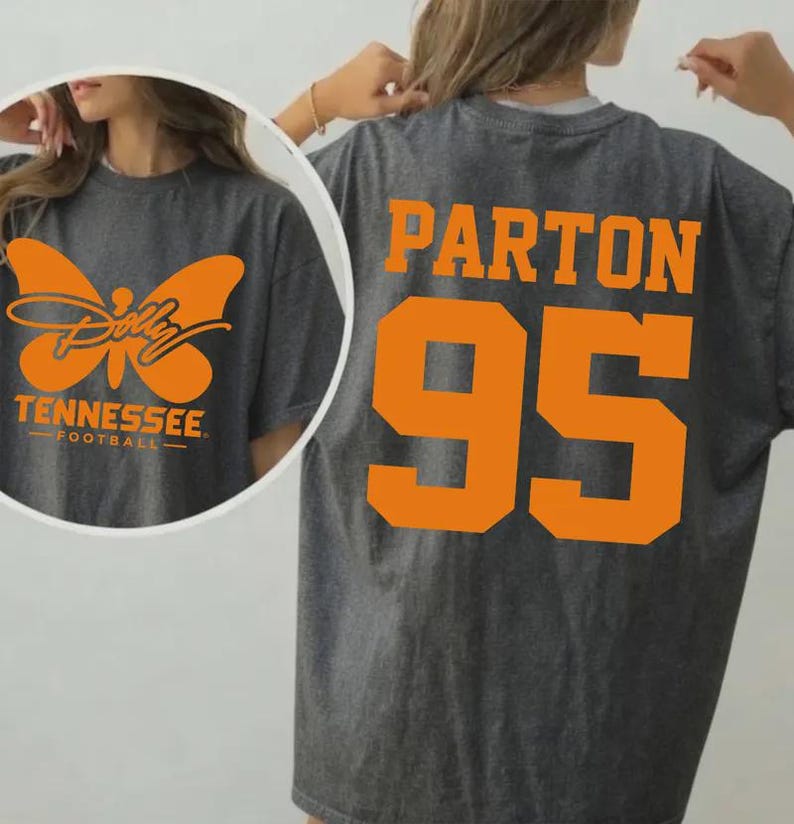 May include: A dark gray t-shirt featuring orange graphics. The back displays the text PARTON above the number 95 in a bold font. The front circular inset shows an orange butterfly graphic with the text Dolly Tennessee Football.