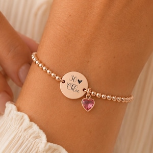 Op de afbeelding: Een armband van roségoudkleurige kraaltjes met een ronde bedel gegraveerd met het getal 30, een klein hartsymbool en de naam Chloe in een sierlijk lettertype. Een kleine, roze, hartvormige edelsteen hangt aan de ronde schijf.