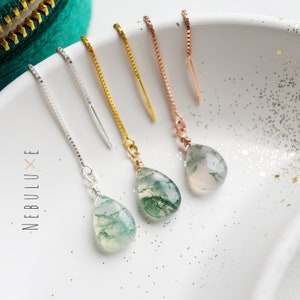 May include: Three pairs of dangle earrings with green moss agate teardrop stones. The earrings are available in silver, gold, and rose gold chain styles.