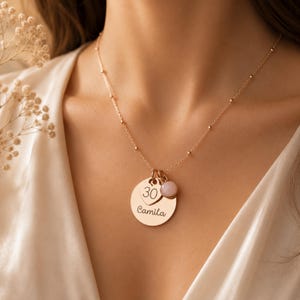 Peut inclure: Un collier couleur or rose compos&eacute; d'une fine cha&icirc;ne perl&eacute;e, d'un pendentif circulaire grav&eacute; du pr&eacute;nom Camila, d'une petite breloque en forme de c&oelig;ur grav&eacute;e du nombre 30 et d'une breloque ronde en pierre rose p&acirc;le.