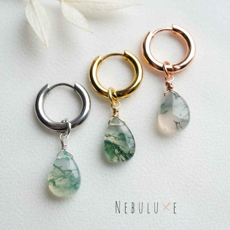 May include: Three hoop earrings with a teardrop-shaped green moss agate pendant hanging from each. The hoops are silver, gold, and rose gold.
