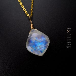 May include: A gold chain necklace with a large, iridescent moonstone pendant. The pendant is faceted and has a blue and white color.