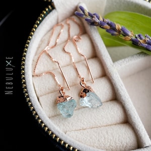 May include: A pair of rose gold aquamarine crystal earrings with delicate chain drop designs. The earrings are displayed in a black velvet jewellery box.