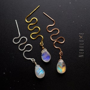 Könnte beinhalten: Drei Paar Ohrringe mit schimmernden Mondstein-Tropfenanhängern. Die Ohrringe haben eine zarte Kette in Silber, Gold und Roségold.