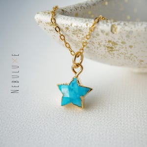 Puede incluir: Un collar de cadena dorada con un colgante de estrella turquesa.