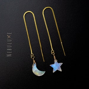 May include: A pair of gold chain earrings with moon and star charms made of iridescent moonstone.