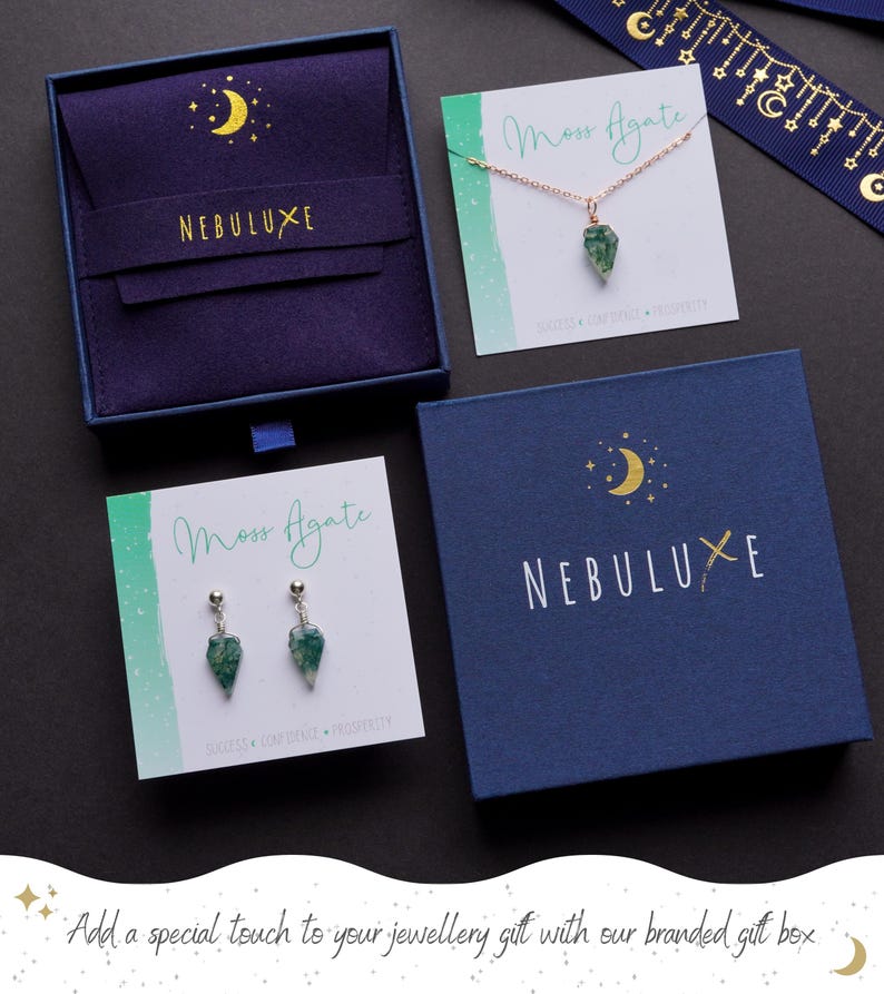 May include: An assortment of jewelry and gift boxes. The image features a necklace and earrings with green stone pendants, displayed on cards that read "Moss Agate." The boxes are navy blue with gold crescent moon and star designs, and the brand name "NEBULUXE."