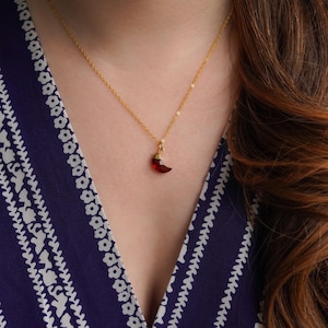 Pode incluir: Um colar de corrente de ouro com um pingente de pimenta vermelha. O pingente é feito de vidro e tem um acabamento dourado.