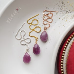 Peut inclure: Trois paires de boucles d'oreilles avec des pierres précieuses violettes en forme de goutte et des extensions de chaîne délicates. Les chaînes sont en argent, en or et en or rose.