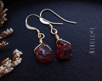 May include: A pair of gold earrings with red gemstone drops. The earrings are made with raw, unpolished stones and have a simple, minimalist design.
