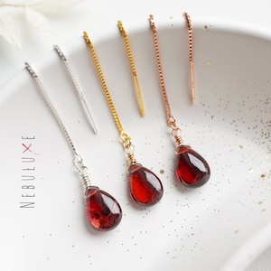 Könnte beinhalten: Drei Paar Ohrringe mit roten Edelstein-Tropfen. Die Ohrringe haben eine Kette mit einer kleinen Metallstange oben und einem tropfenförmigen roten Edelstein unten. Die Ketten sind silber, gold und roségold.