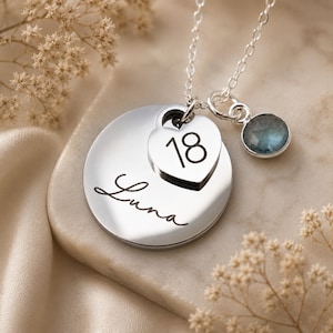 Peut inclure: Un collier argent&eacute; compos&eacute; d'un pendentif circulaire grav&eacute; du pr&eacute;nom Luna en &eacute;criture cursive, d'une breloque en forme de c&oelig;ur grav&eacute;e du nombre 18 et d'une petite breloque ronde orn&eacute;e d'une pierre pr&eacute;cieuse bleue &agrave; facettes sur la cha&icirc;ne.