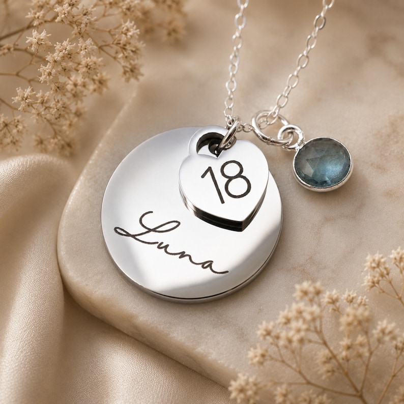 Peut inclure: Un collier argent&eacute; compos&eacute; d'un pendentif circulaire grav&eacute; du pr&eacute;nom Luna en &eacute;criture cursive, d'une breloque en forme de c&oelig;ur grav&eacute;e du nombre 18 et d'une petite breloque ronde orn&eacute;e d'une pierre pr&eacute;cieuse bleue &agrave; facettes sur la cha&icirc;ne.