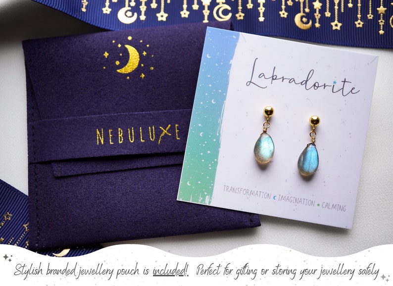 May include: A pair of gold labradorite earrings with a teardrop shape. The earrings are displayed on a card with the text "Labradorite" and "Transformation Imagination Calming". A blue velvet pouch with the text "NEBULUXE" is included.