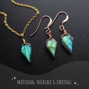May include: A matching jewelry set featuring a necklace and earrings. The necklace has a gold chain with a pendant of a faceted, blue-green gemstone. The earrings have copper-colored hooks and matching gemstone pendants. The text "MATCHING NECKLACE & EARRINGS" is at the bottom.