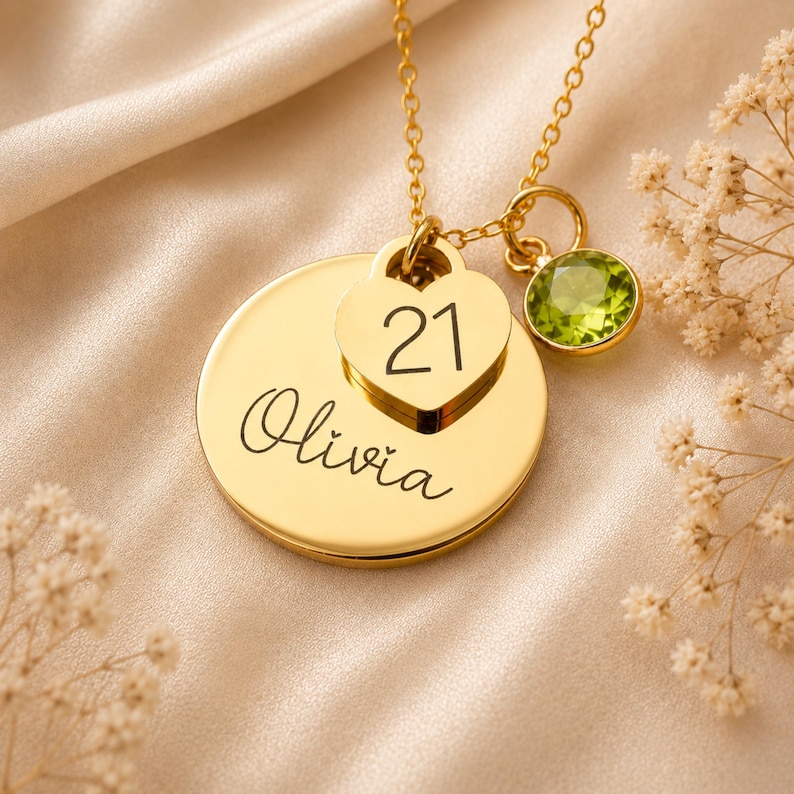 Peut inclure: Un collier dor&eacute; compos&eacute; d'un pendentif circulaire grav&eacute; du pr&eacute;nom Olivia, d'une breloque en forme de c&oelig;ur grav&eacute;e du nombre 21 et d'une pierre pr&eacute;cieuse ronde &agrave; facettes vert citron, le tout suspendu &agrave; une fine cha&icirc;ne dor&eacute;e.