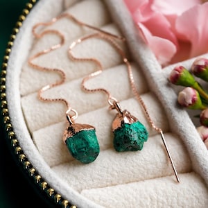 Może przedstawiać: Para kolczyków wiszących z różowego złota z zielonymi kroplami malachitu. Kolczyki są prezentowane w pudełku na biżuterię z zielonym tłem.