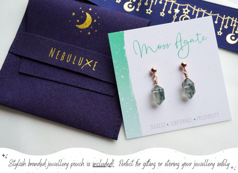 May include: A pair of moss agate earrings with rose gold wire wrapped around the stones. The earrings are on a white card with the text "Moss Agate" and "SUCCESS CONFIDENCE PROSPERITY". The earrings are packaged in a blue velvet pouch with a gold crescent moon and stars design and the text "NEBULUXE".