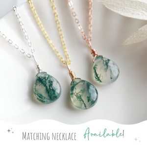 May include: Three delicate necklaces with moss agate pendants. The necklaces are available in silver, gold, and rose gold chains. The moss agate stones are a light green color with dark green veins.