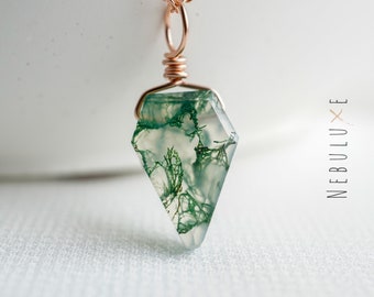 May include: A delicate necklace featuring a green moss agate pendant with a rose gold chain. The pendant is a faceted, diamond-shaped stone with intricate green patterns.