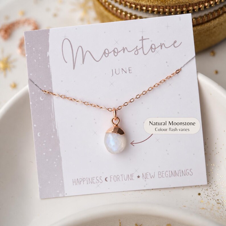 May include: A rose gold chain necklace with a single oval moonstone pendant. The jewellery is displayed on a white card featuring the text Moonstone, JUNE, and HAPPINESS, FORTUNE, NEW BEGINNINGS, with a note stating Natural Moonstone Colour flash varies.