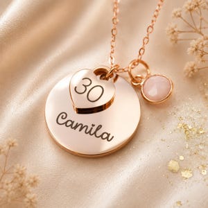 Peut inclure: Un collier couleur or rose compos&eacute; d'un pendentif circulaire grav&eacute; du pr&eacute;nom Camila, d'une breloque en forme de c&oelig;ur grav&eacute;e du nombre 30 et d'une petite breloque ronde orn&eacute;e d'une pierre rose p&acirc;le &agrave; facettes fix&eacute;e &agrave; la cha&icirc;ne.