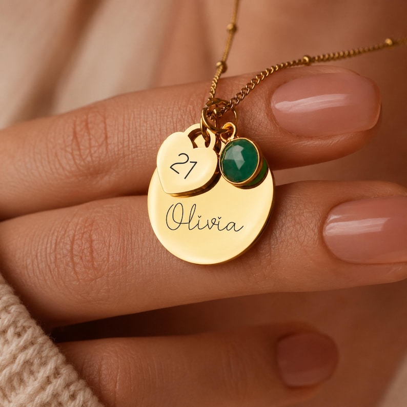 Peut inclure: Un collier dor&eacute; compos&eacute; d'un pendentif circulaire grav&eacute; du pr&eacute;nom Olivia, d'une breloque en forme de c&oelig;ur grav&eacute;e du nombre 21 et d'une petite pierre pr&eacute;cieuse verte ronde, le tout suspendu &agrave; une fine cha&icirc;ne de couleur dor&eacute;e.