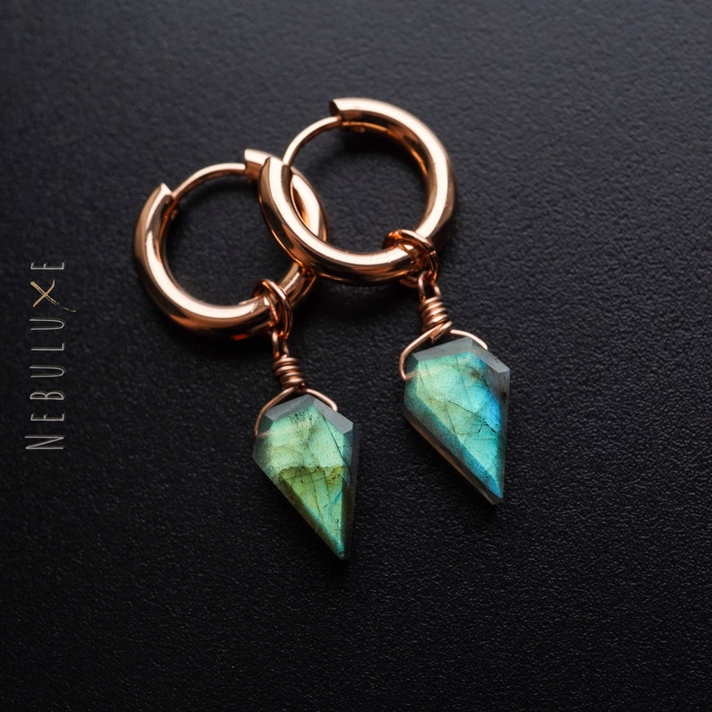 May include: Rose gold hoop earrings with faceted, teardrop-shaped labradorite pendants. The gemstones display green and blue iridescence. The word "NEBULUXE" is printed vertically on the left side of the image.