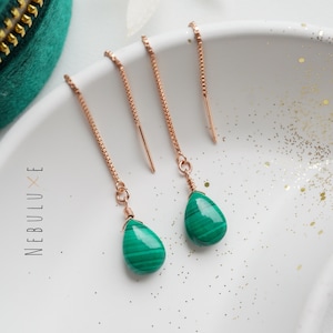 May include: A pair of rose gold earrings with green malachite teardrop stones hanging from delicate chains.