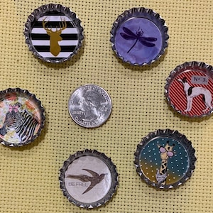 May include: Six different bottle cap magnets with various designs. The designs include a deer, a dragonfly, a zebra, a giraffe, a bird, and a dog. The magnets are all silver and have a black rim.