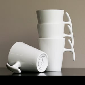 May include: Four white ceramic mugs with unique antler-shaped handles. The mugs are stacked on top of each other. The bottom mug has the text "371 Carsten Design" printed on the bottom.