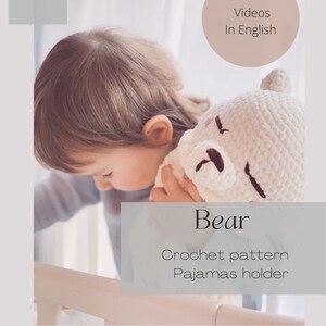 Puede incluir: Un oso blanco de crochet con ojos marrones y una nariz negra. El oso est&aacute; siendo sostenido por un ni&ntilde;o. La imagen incluye el texto "Bear Crochet pattern Pajamas holder" y "22 Videos In English".