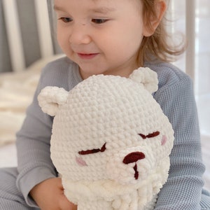 Puede incluir: Un ni&ntilde;o peque&ntilde;o con una camisa de manga larga azul claro sostiene un animal de peluche blanco de crochet que se parece a un oso. El oso tiene una nariz marr&oacute;n y mejillas rosadas.