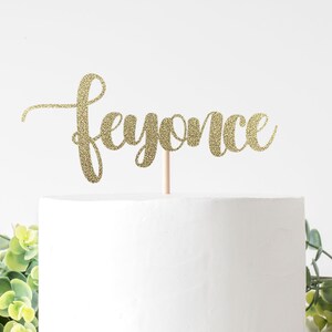 May include: Gold glitter cake topper with the word "Beyonce" written in cursive.
