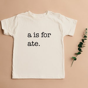 May include: A white t-shirt with the text "a is for ate." printed in black on the front.