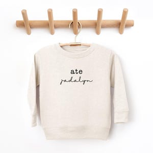 May include: A cream colored sweatshirt with the text "ate Jadaly" in black.