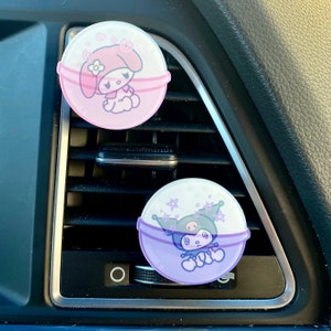 May include: Two car air fresheners, one pink with a cartoon character and the other purple with a cartoon character. Both are round and have a floral design.
