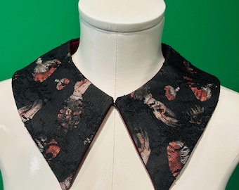 May include: A black lace collar with a red lining, displayed on a white mannequin. The collar features a repeating pattern of red and beige floral and bird designs. The collar is a fashion accessory.